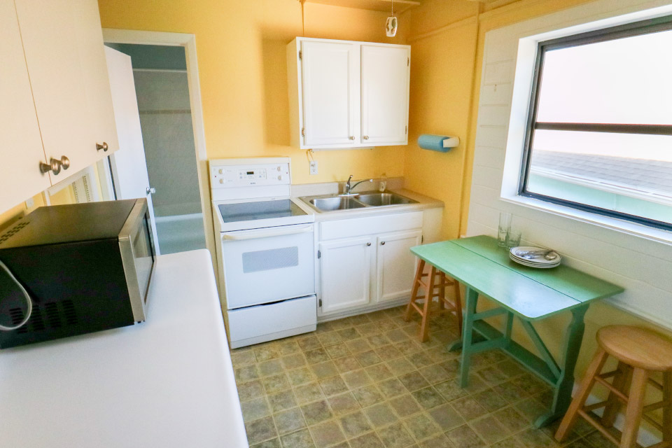 photograph of kitchen showing oven, sink, table, chairs, dishes, and microwave